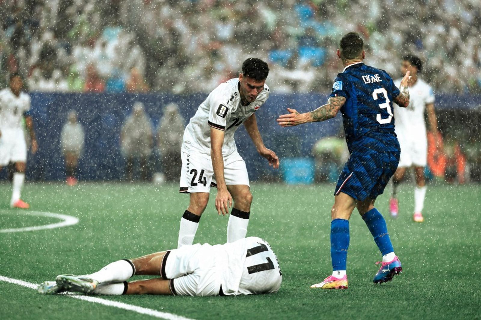Lucas Digne reacts in the rain as an Iraq player lies on the pitch during a weather-hit World Cup match