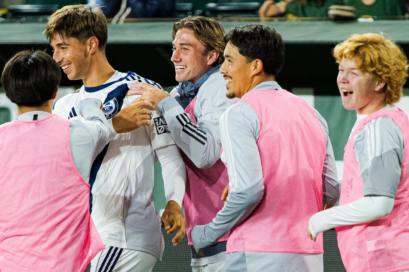 Ventura County FC substitutes in pink training bibs celebrate with a teammate in white on the sideline at Providence Park on October 25, 2026.