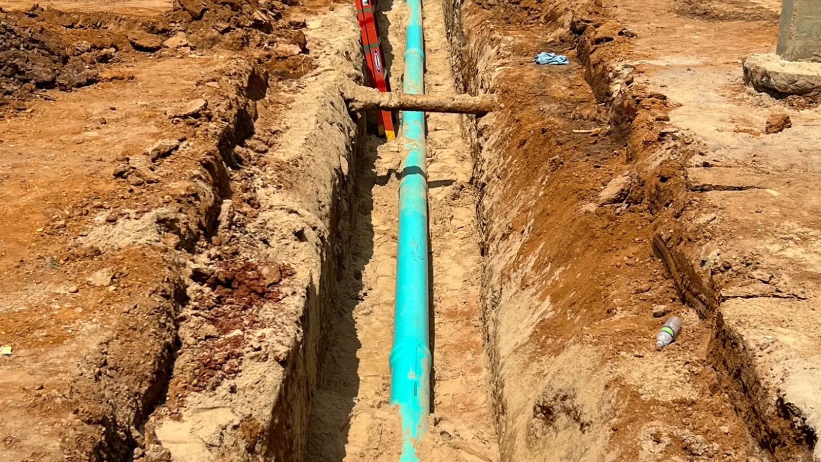 A length of pipe laid along the bottom of an open dirt trench at a construction site
