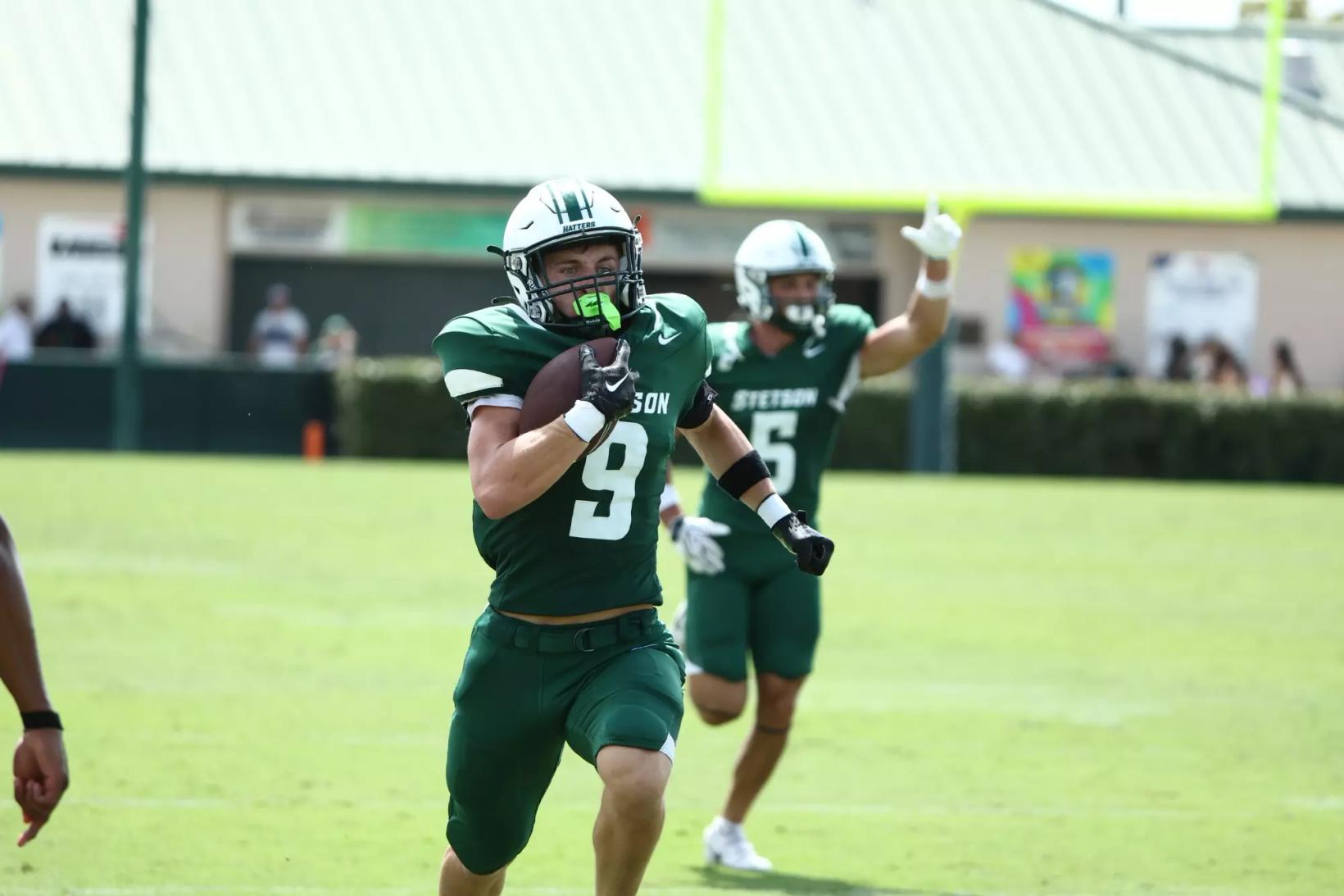 Stetson's No. 9 in a green home jersey runs with the football as teammate No. 5 celebrates behind at Spec Martin Stadium in DeLand, Fla., during a 2026 Stetson home game (file photo).