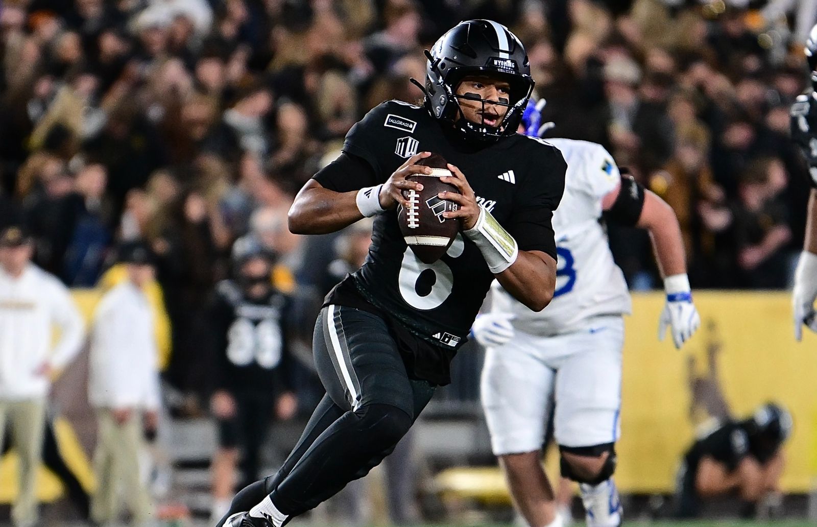 Wyoming quarterback Tyler Hughes, No. 6 in a black uniform, rolls out with the ball as an Air Force player in white trails during Wyoming's 28-14 win on Oct. 23, 2026.