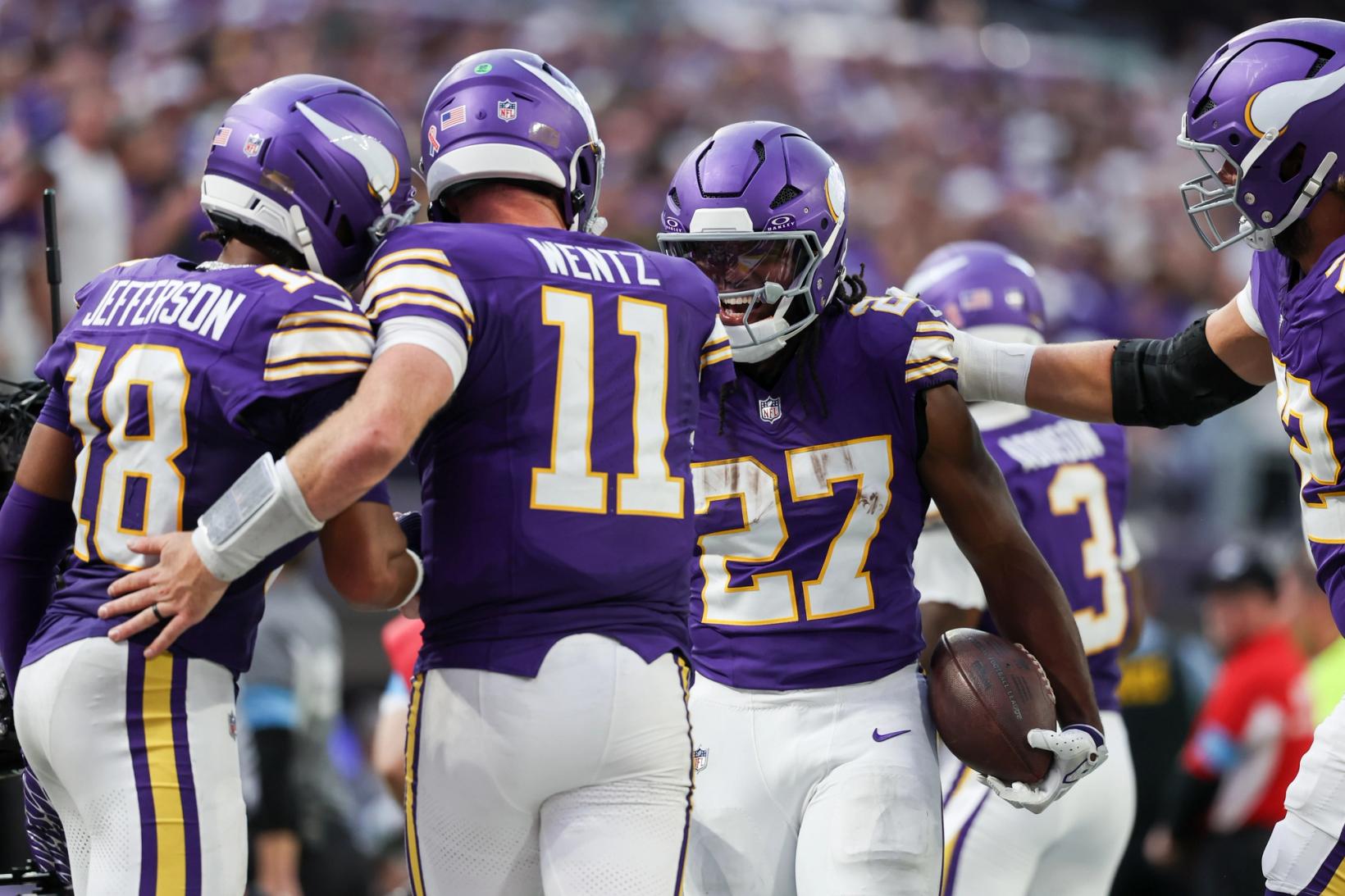Minnesota Vikings quarterback Carson Wentz (11) wraps an arm around wide receiver Justin Jefferson (18) while running back Jordan Mason (27) celebrates holding the football.