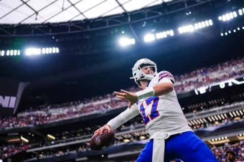 Buffalo Bills quarterback Josh Allen (17) winds up to throw beneath the stadium lights, with a packed crowd behind him.