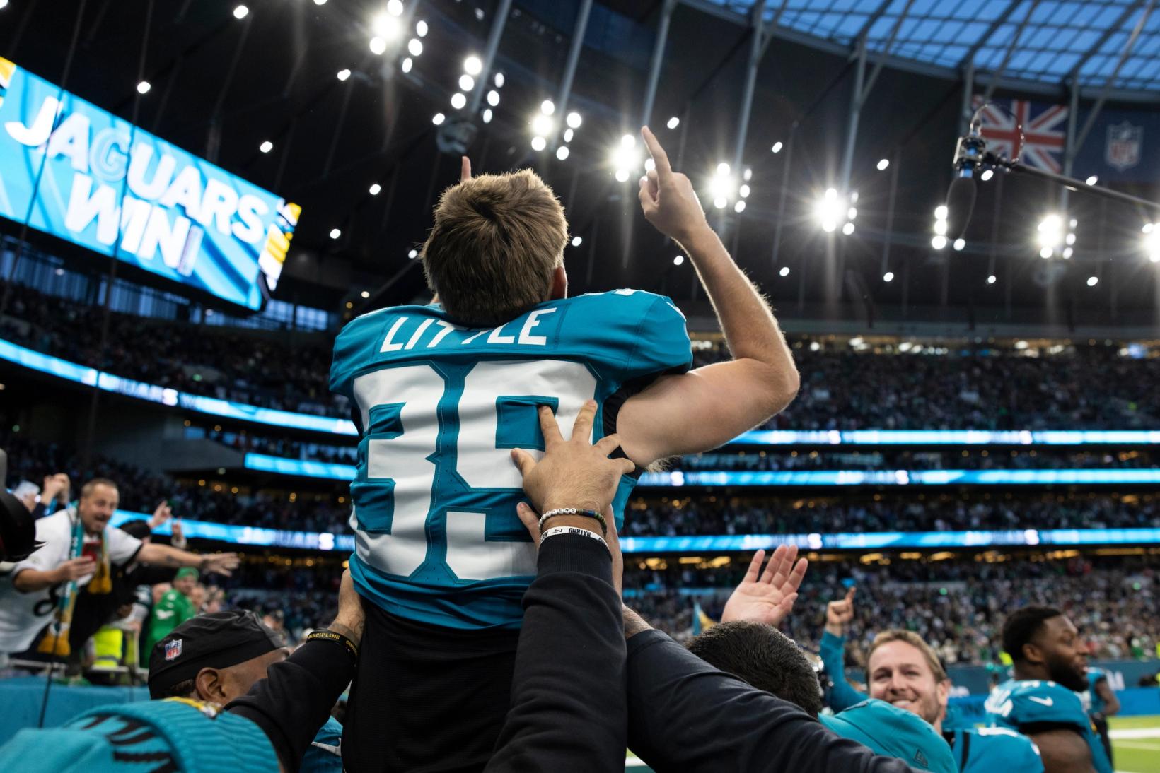 Jacksonville Jaguars kicker Cam Little (39) points skyward as teammates lift him up and the video board reads Jaguars Win at Tottenham Hotspur Stadium in London