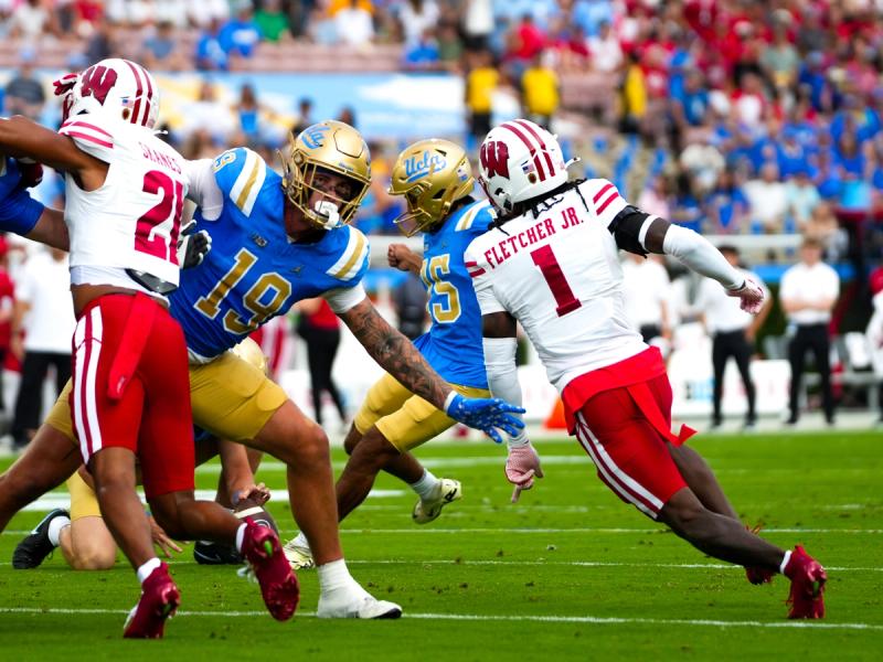 UCLA player carries the ball against Wisconsin defenders Fletcher Jr. and others at the Rose Bowl — Photo Credit: Steven Kwang/Undrafted