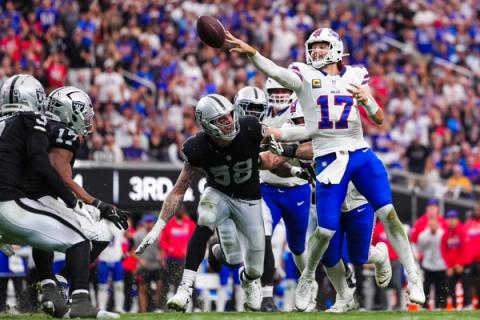 Buffalo Bills quarterback Josh Allen (17) flips a pass as Las Vegas Raiders defender Maxx Crosby (98) lunges toward him at Allegiant Stadium.