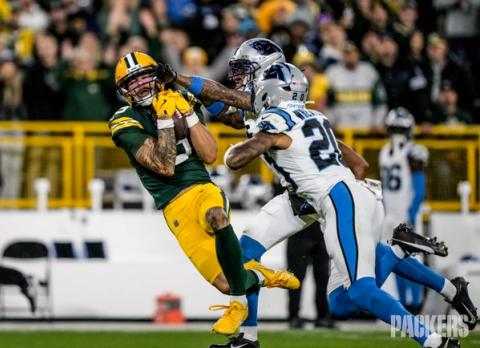 A Green Bay Packers receiver clutches the ball to his chest for a catch as two Carolina Panthers defenders, one wearing No. 20, converge on him at Lambeau Field.