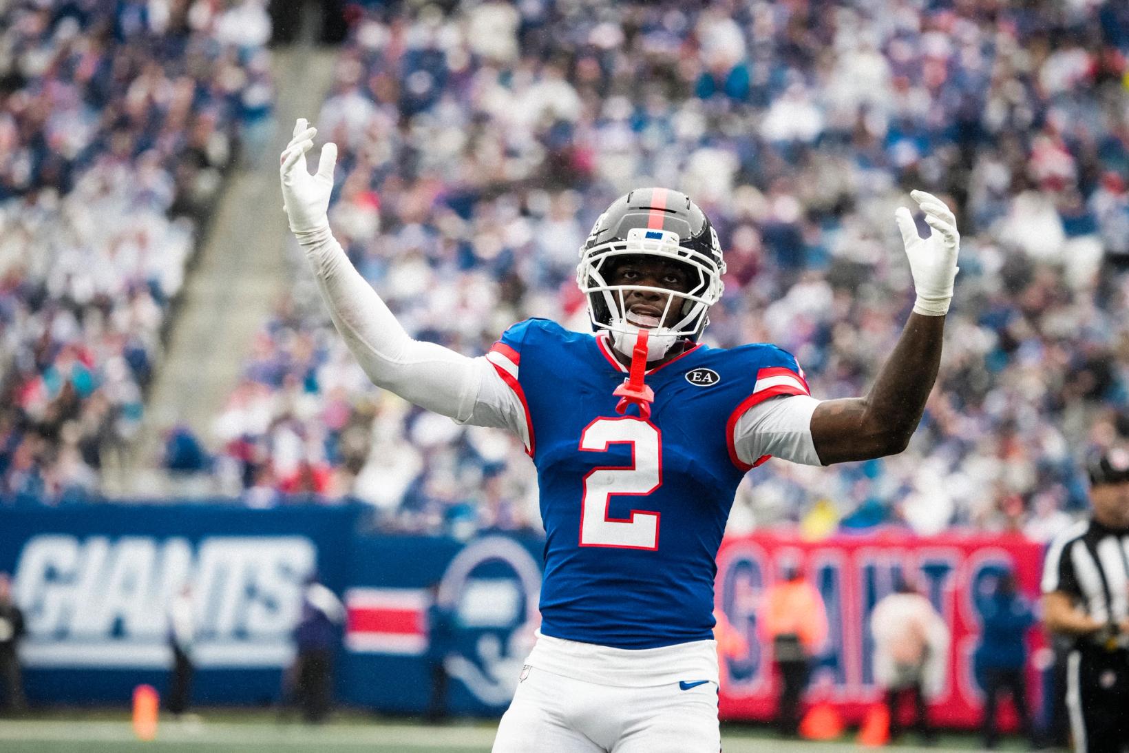 New York Giants cornerback Deonte Banks (2) raises both arms toward the crowd in front of Giants signage.
