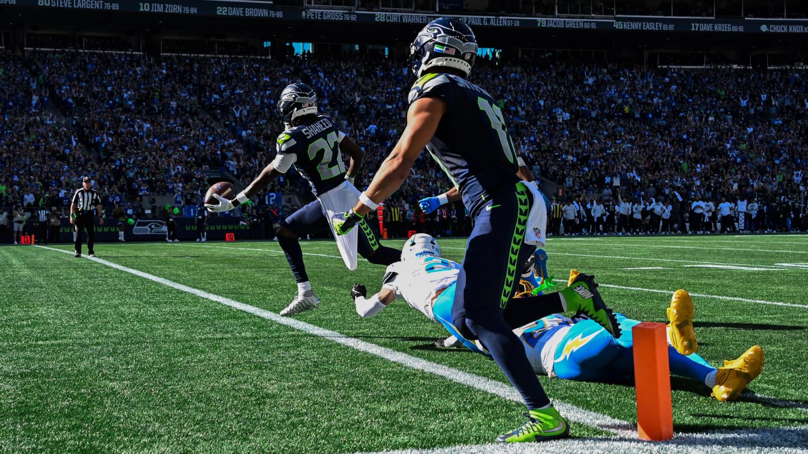 Seattle Seahawks' Rashid Shaheed (22) holds the ball out as he runs past the pylon while a Los Angeles Chargers defender dives and a Seahawks teammate blocks in the foreground at Lumen Field