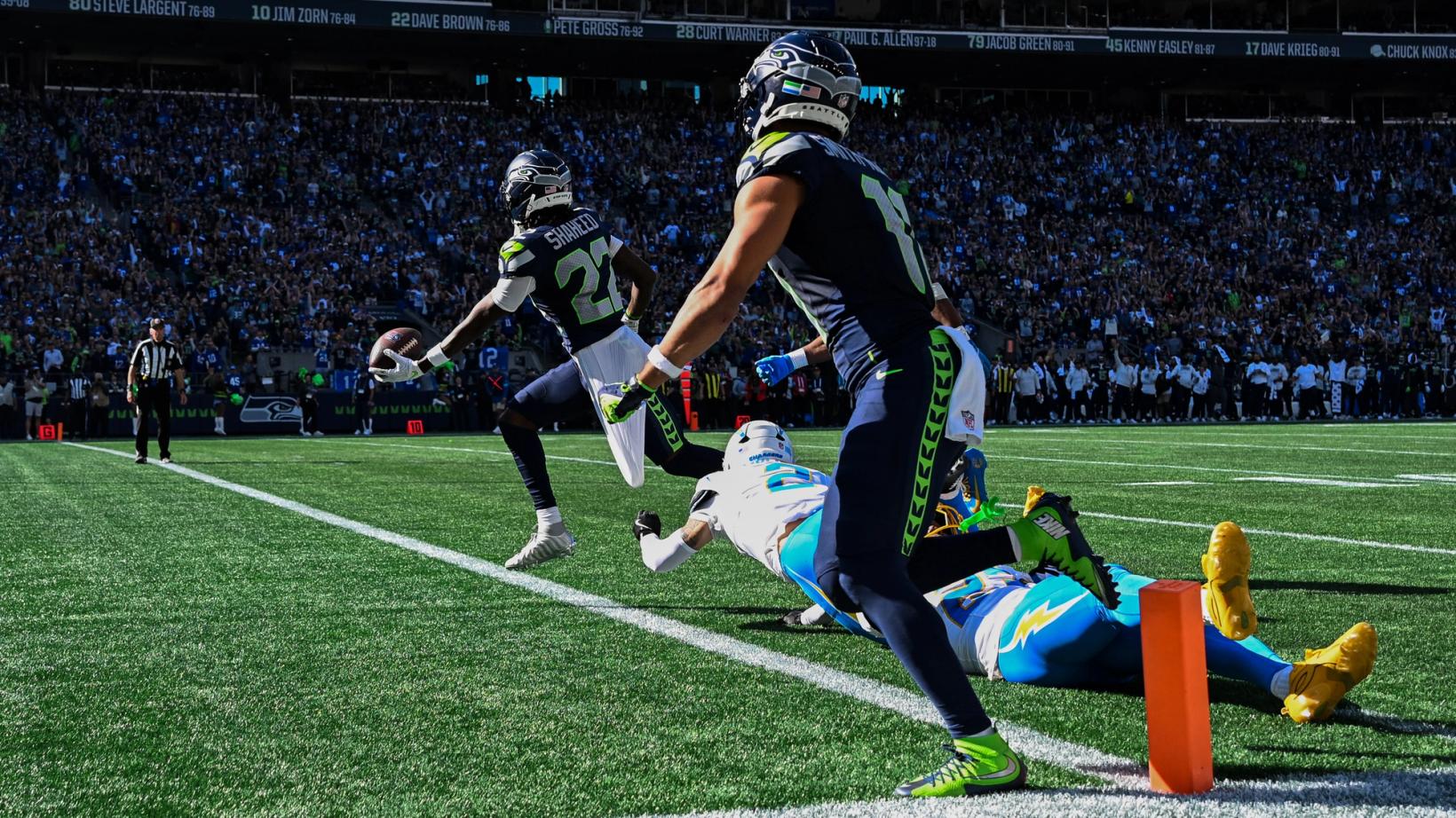 Seattle Seahawks' Rashid Shaheed (22) holds the ball out as he runs past the pylon while a Los Angeles Chargers defender dives and a Seahawks teammate blocks in the foreground at Lumen Field