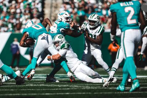 Miami Dolphins running back Ollie Gordon II (0) carries the ball as New York Jets defender Dane Belton (6) dives to tackle him and quarterback Malik Willis (2) looks on at MetLife Stadium.