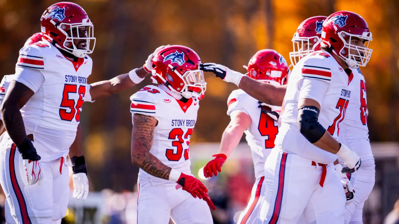 Stony Brook players in white road uniforms and red helmets celebrate with a teammate wearing No. 33 during the Seawolves' 27-17 win at Bryant on Oct. 24, 2026