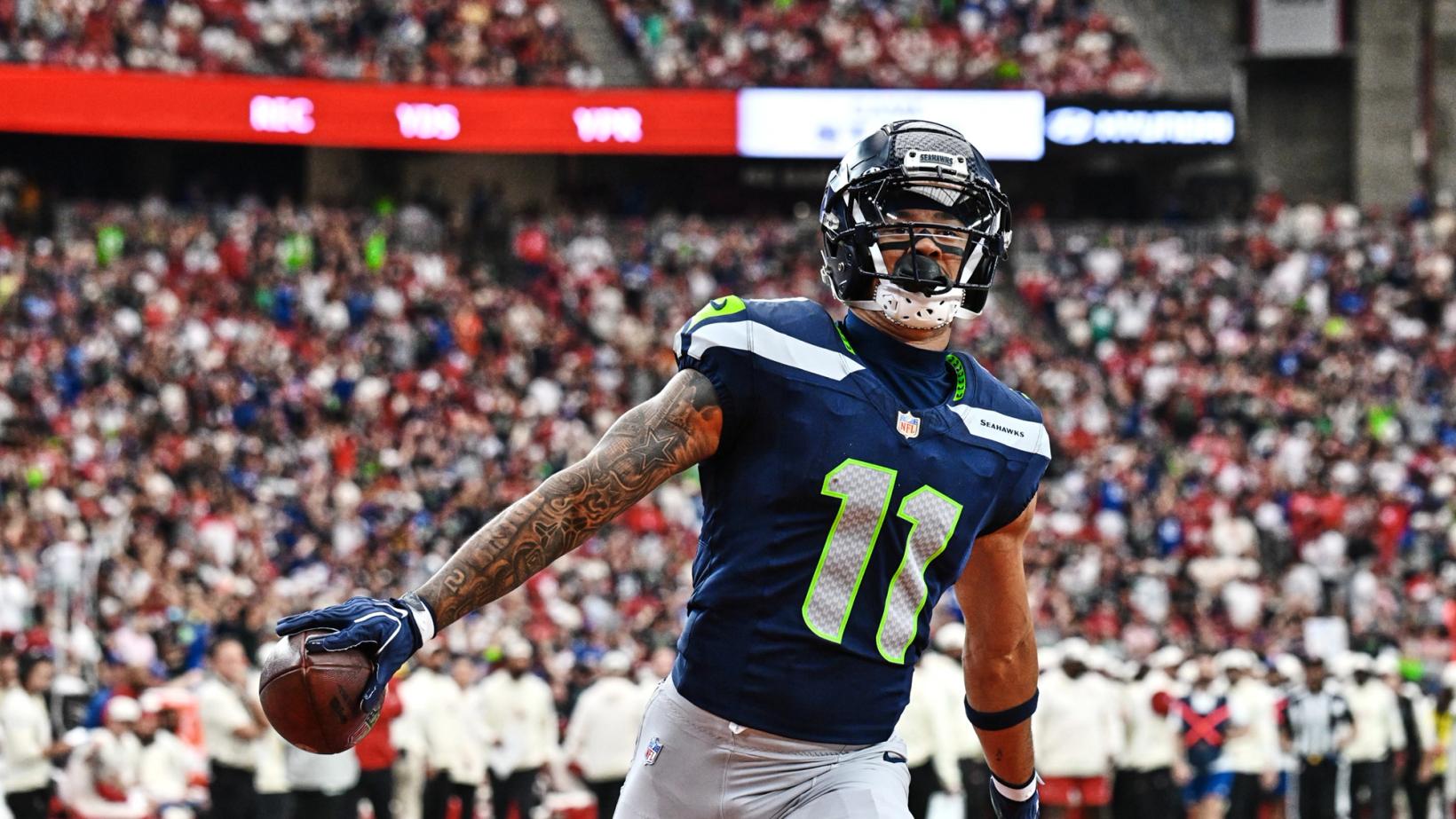 Seattle Seahawks receiver Jaxon Smith-Njigba (11) holds the football out in one hand as he celebrates in front of the crowd at State Farm Stadium