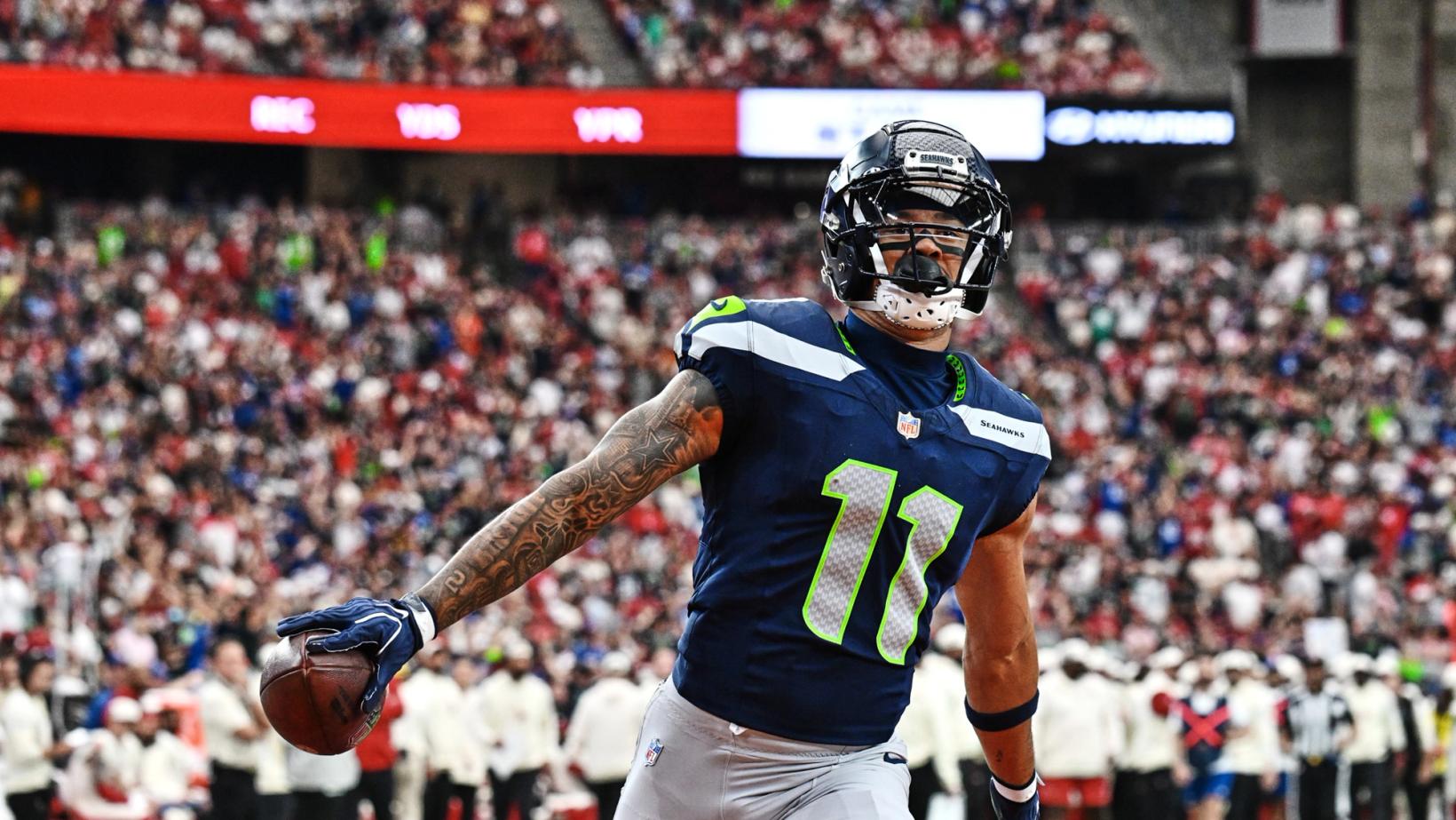 Seattle Seahawks receiver Jaxon Smith-Njigba (11) holds the football out in one hand as he celebrates in front of the crowd at State Farm Stadium