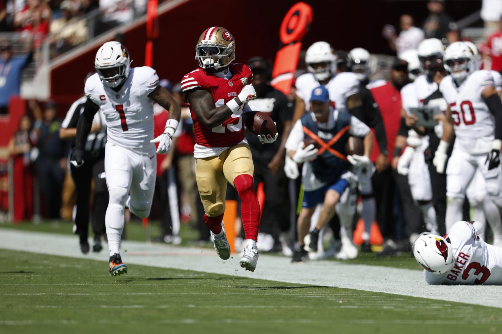 San Francisco 49ers wide receiver Deebo Samuel Sr. runs down the sideline with the football as Arizona Cardinals' Mack Wilson Sr. (1) chases and Budda Baker (3) lies on the turf at Levi's Stadium.