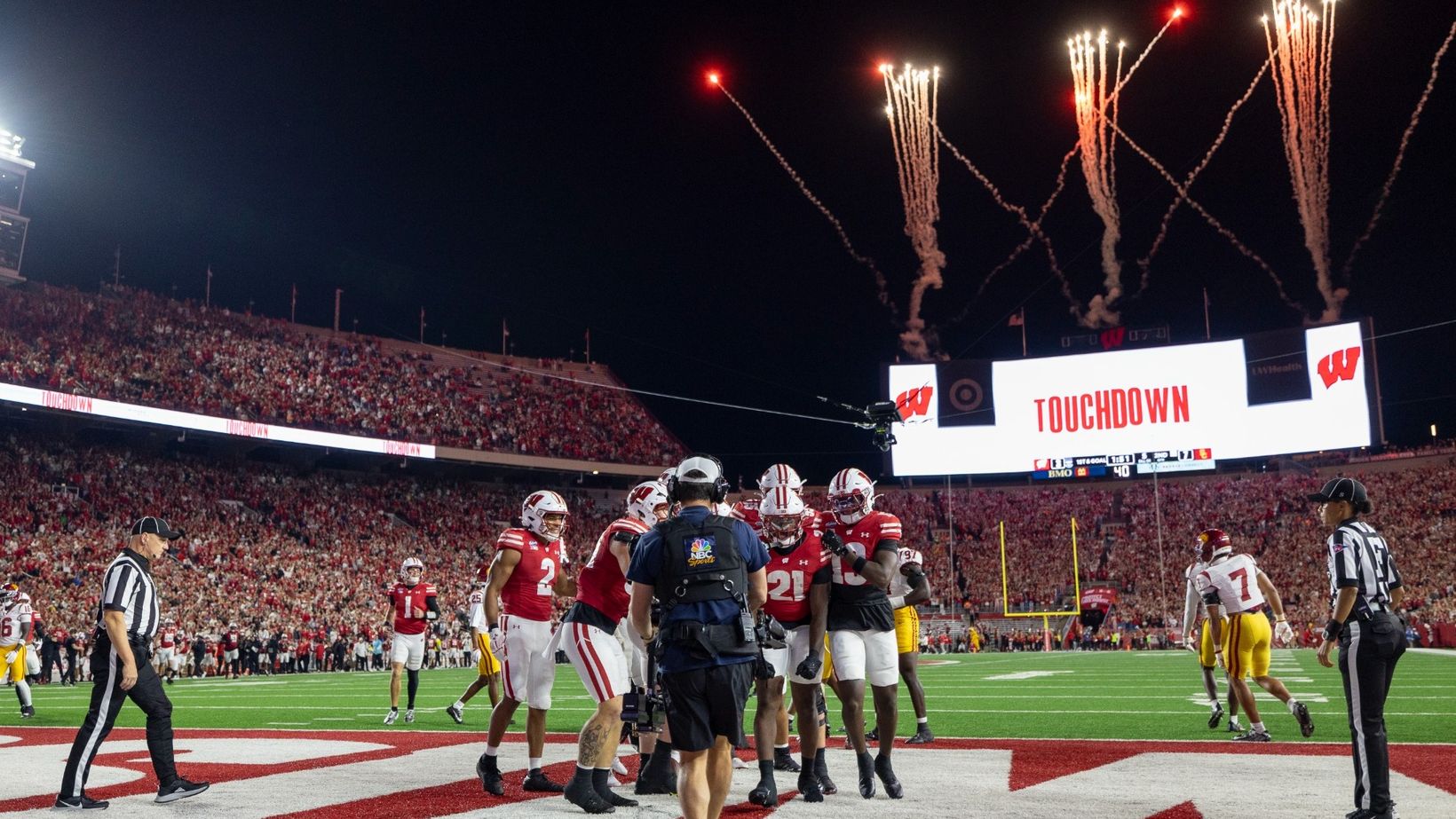 Wisconsin players in red jerseys celebrate a touchdown in the end zone as fireworks go off and the Camp Randall Stadium video board reads Touchdown during the Badgers' 24-7 win over USC on Oct. 24, 2026, in Madison