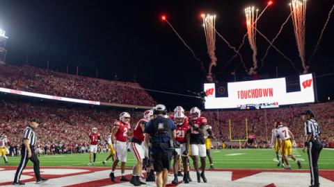 Wisconsin players in red jerseys celebrate a touchdown in the end zone as fireworks go off and the Camp Randall Stadium video board reads Touchdown during the Badgers' 24-7 win over USC on Oct. 24, 2026, in Madison