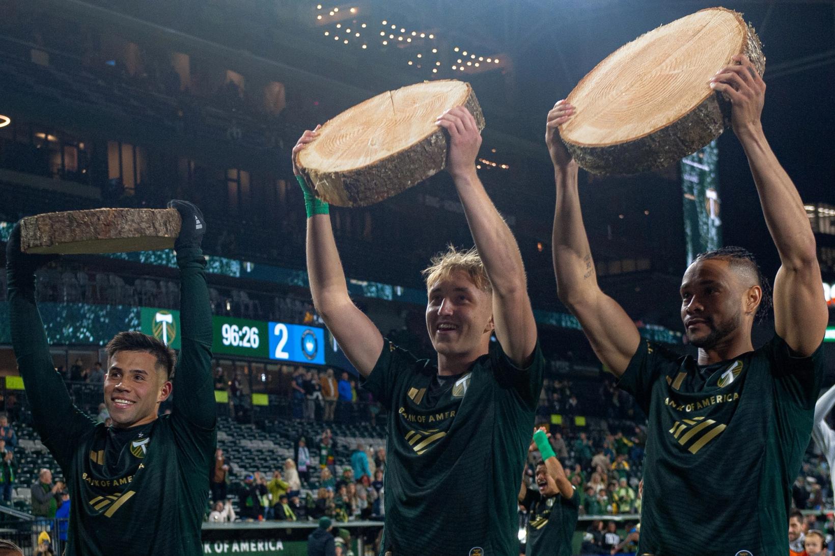 Portland Timbers players hoist log slices overhead in celebration at Providence Park after the 3-2 win over Charlotte FC on October 24, 2026.