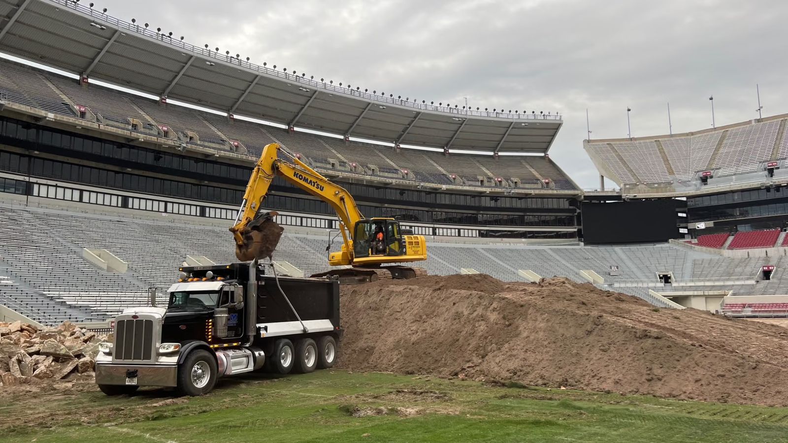 A Komatsu excavator loads soil from the old Bryant-Denny Stadium playing surface into a dump truck during the 2023 field rebuild