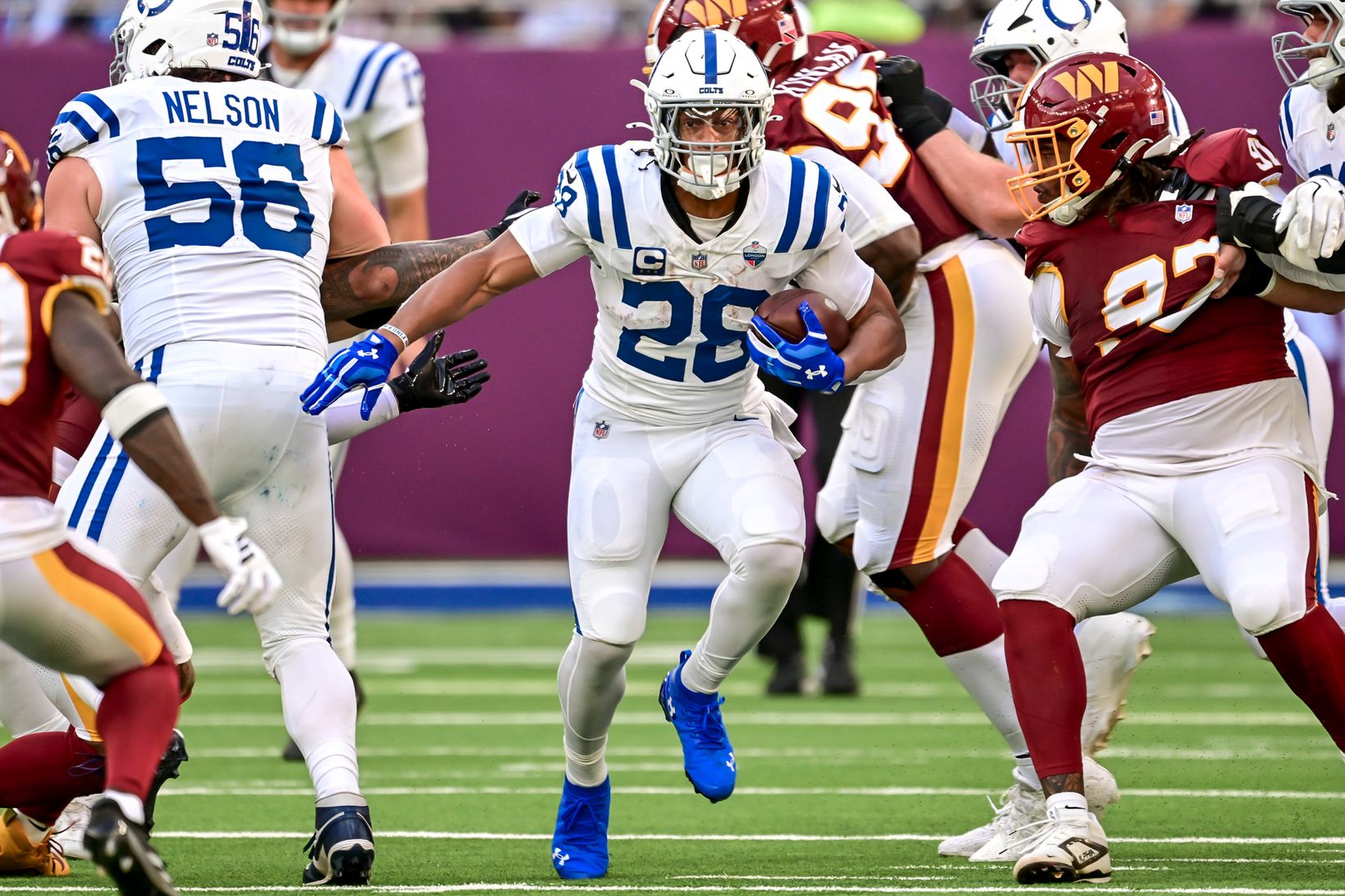 Indianapolis Colts running back Jonathan Taylor (28) carries the ball through a gap as Colts blockers engage Washington Commanders defenders.