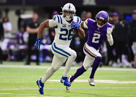 Indianapolis Colts running back Jonathan Taylor, wearing No. 28 and a captain's patch, carries the ball upfield as a Minnesota Vikings defender wearing No. 2 chases him.