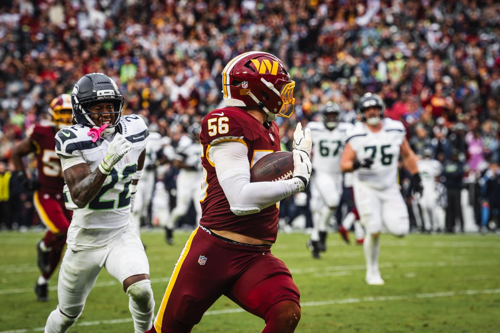 Washington Commanders linebacker Kain Medrano (56) runs with the football as Seattle Seahawks' Rashid Shaheed (22) chases him, with other Seahawks trailing behind.