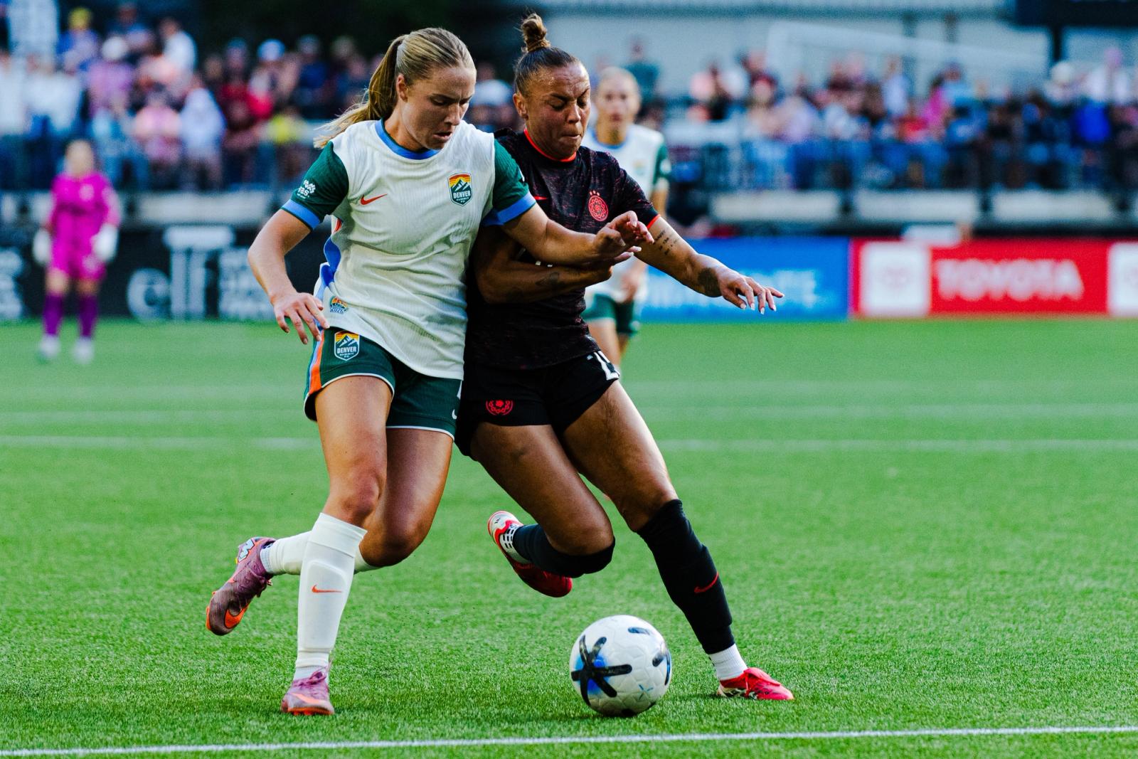 A Denver Summit attacker in the white and green kit battles a Portland Thorns defender in black for the ball during the August 22, 2026 match at Providence Park.