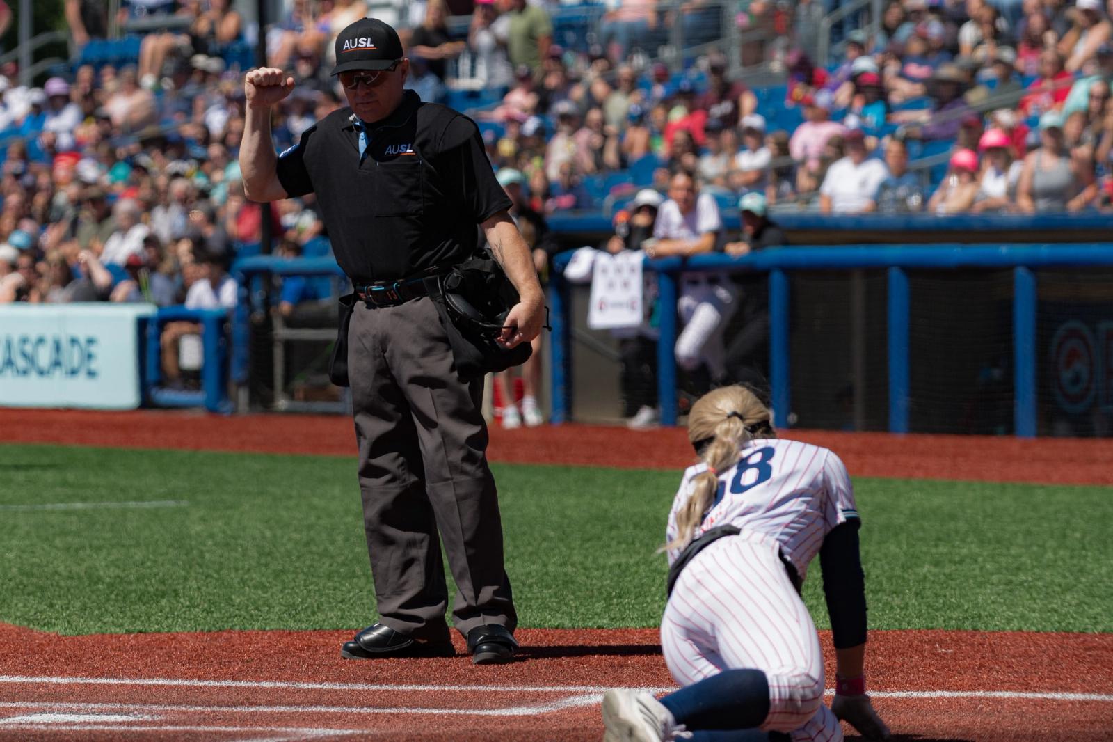 An umpire signals during a play at the base as a Portland Cascade runner goes to the ground, with the Hillsboro Ballpark crowd behind, on July 12, 2026.