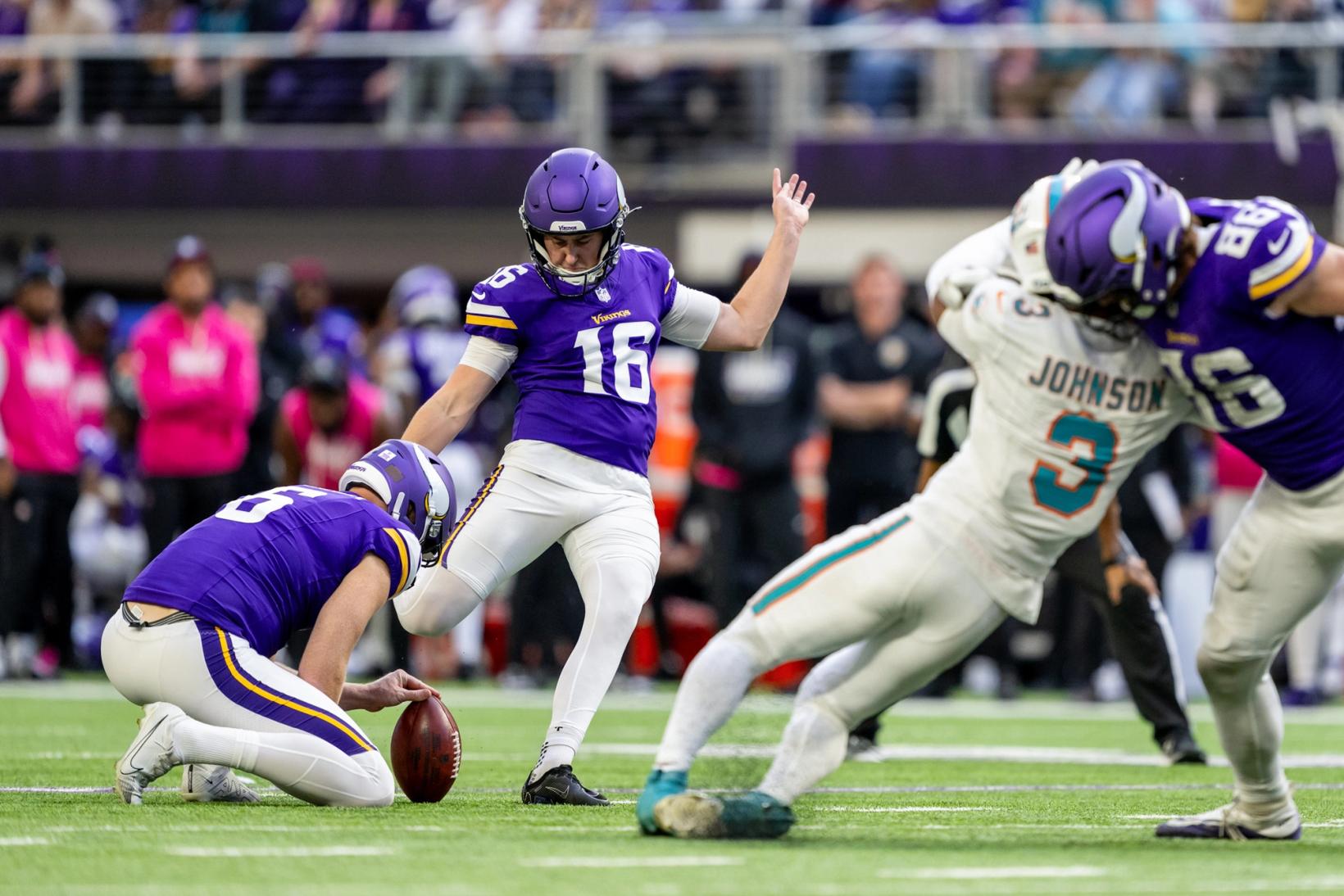 Minnesota Vikings kicker Will Reichard (16) kicks a field goal off a teammate's hold as a Miami Dolphins player lunges in from the right at U.S. Bank Stadium.