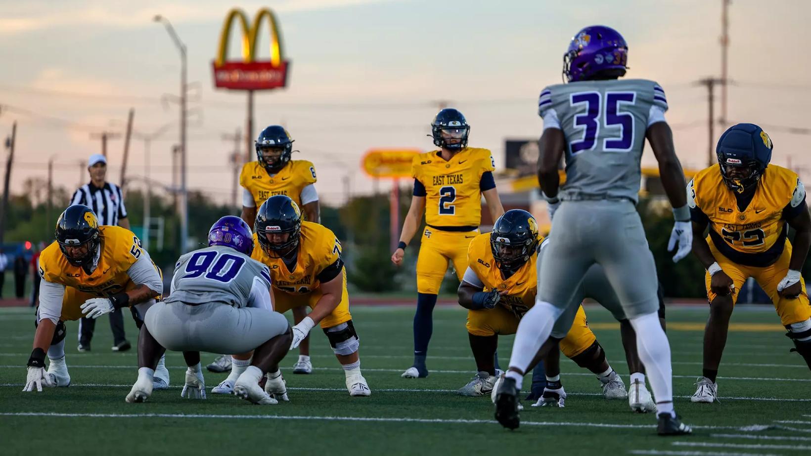 East Texas A&M quarterback Reese Mooney, wearing No. 2 in gold, lines up in the shotgun as Prairie View A&M defenders in gray wait at the line at Memorial Stadium in Commerce