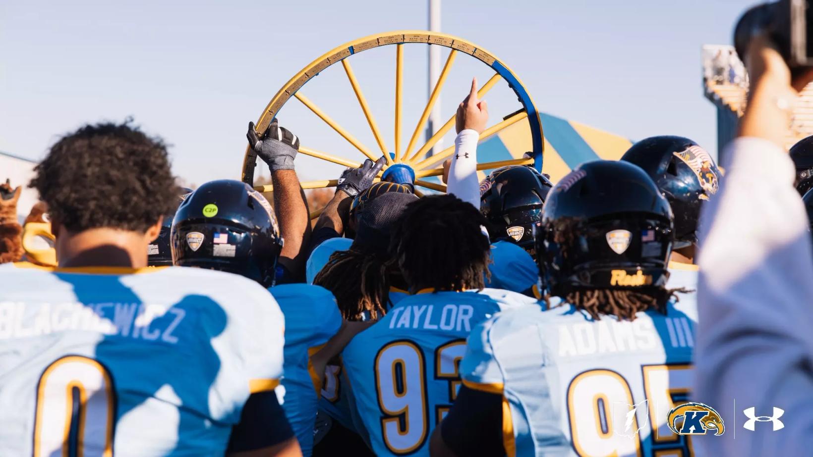 Kent State football players in light blue jerseys gather around and hoist the Wagon Wheel trophy after beating Akron 35-20 at Dix Stadium in Kent, Ohio, on Oct. 24, 2026