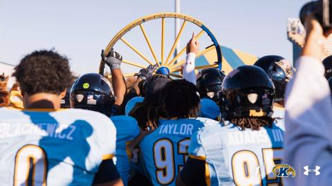 Kent State football players in light blue jerseys gather around and hoist the Wagon Wheel trophy after beating Akron 35-20 at Dix Stadium in Kent, Ohio, on Oct. 24, 2026