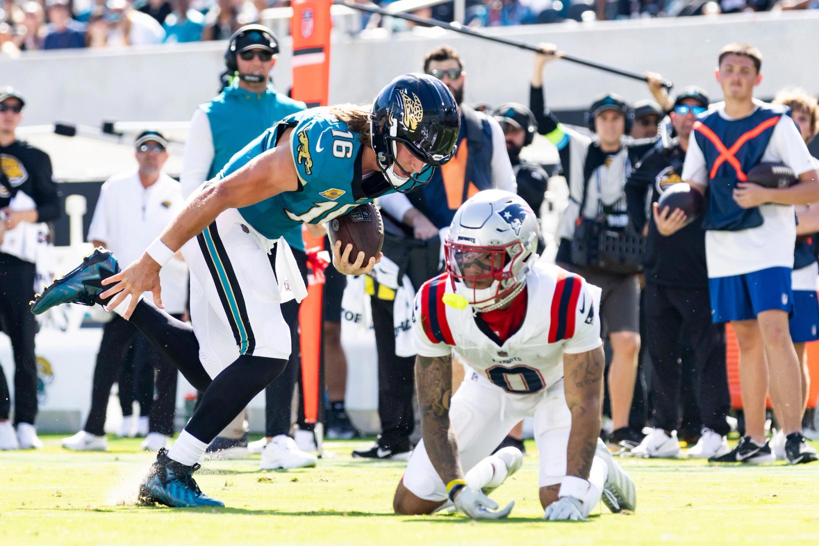 Jacksonville Jaguars quarterback Trevor Lawrence (16) carries the football past New England Patriots' Christian Gonzalez (0), who is on his hands and knees near the sideline.