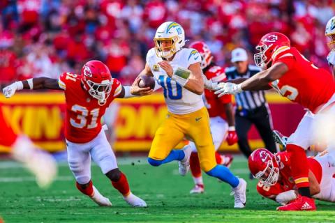 Los Angeles Chargers quarterback Justin Herbert, wearing No. 10, runs with the ball as several Kansas City Chiefs defenders close in around him.
