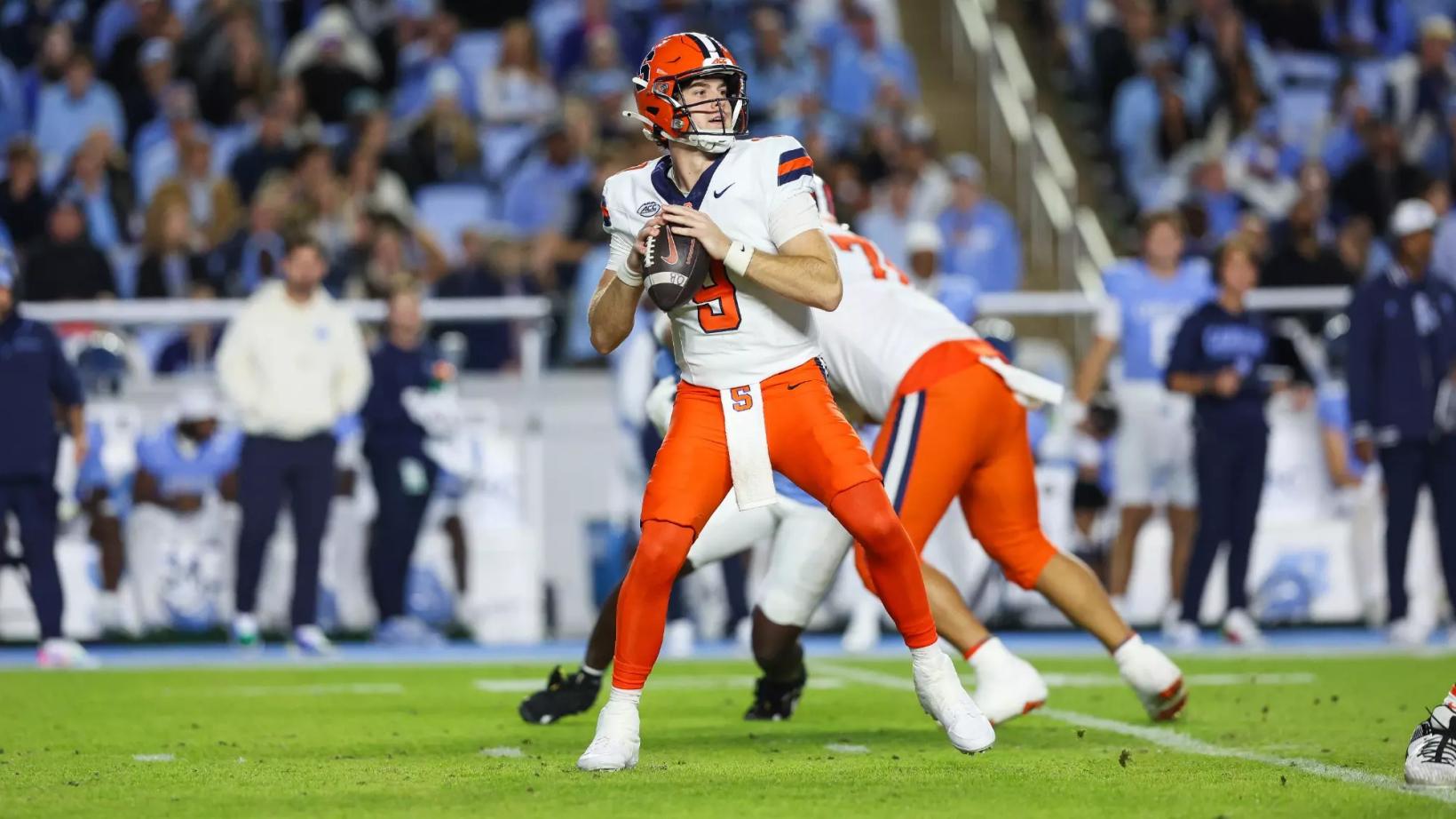 Syracuse quarterback Steve Angeli (5) drops back to pass in a white jersey and orange pants as a lineman blocks, with fans in Carolina blue behind them at Kenan Stadium on Oct. 24, 2026