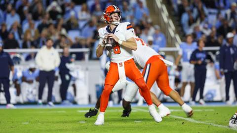 Syracuse quarterback Steve Angeli (5) drops back to pass in a white jersey and orange pants as a lineman blocks, with fans in Carolina blue behind them at Kenan Stadium on Oct. 24, 2026