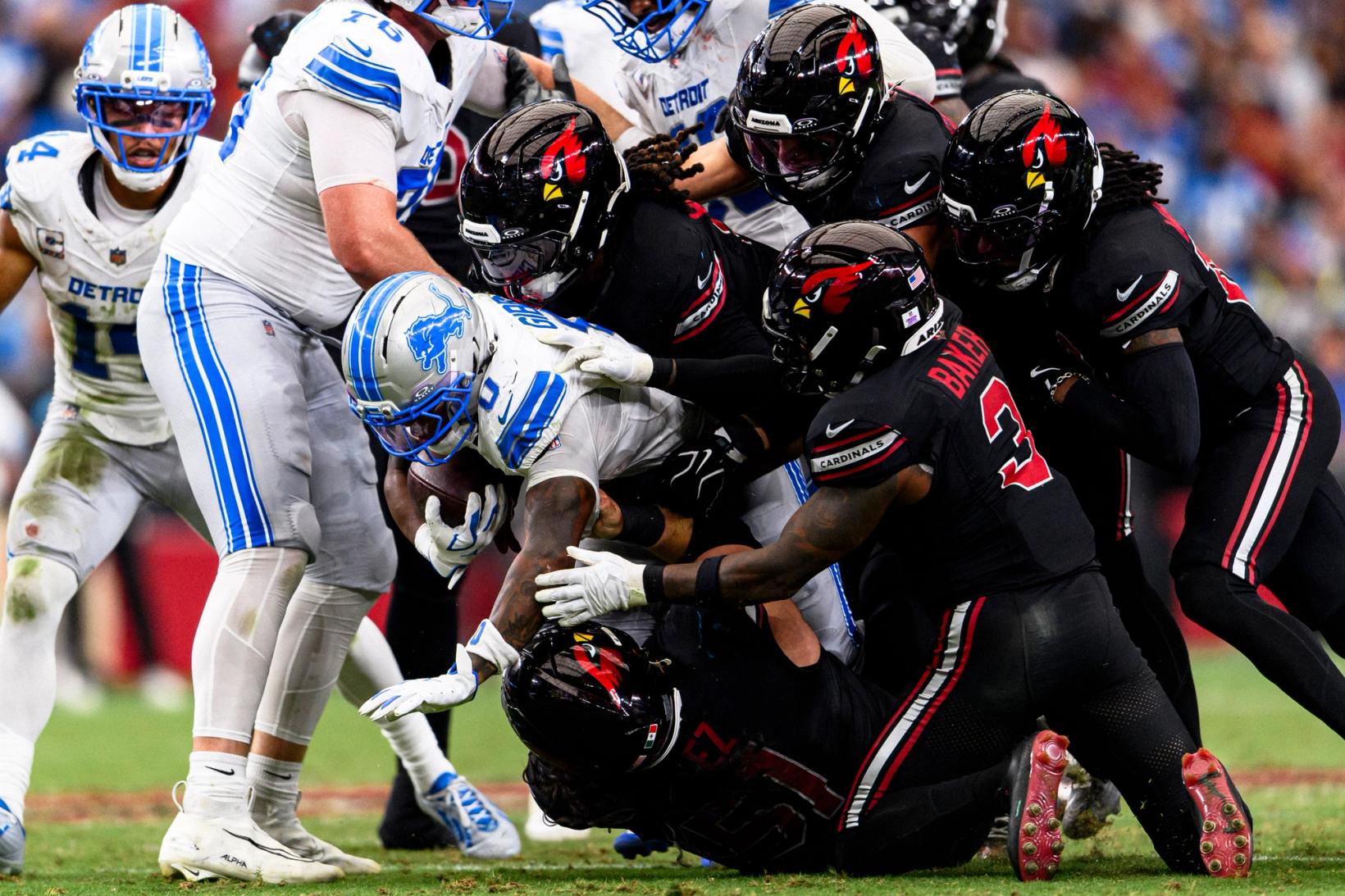 Detroit Lions running back Jahmyr Gibbs (0) drives forward with the ball as Arizona Cardinals safety Budda Baker (3) and several teammates wrap him up at State Farm Stadium.