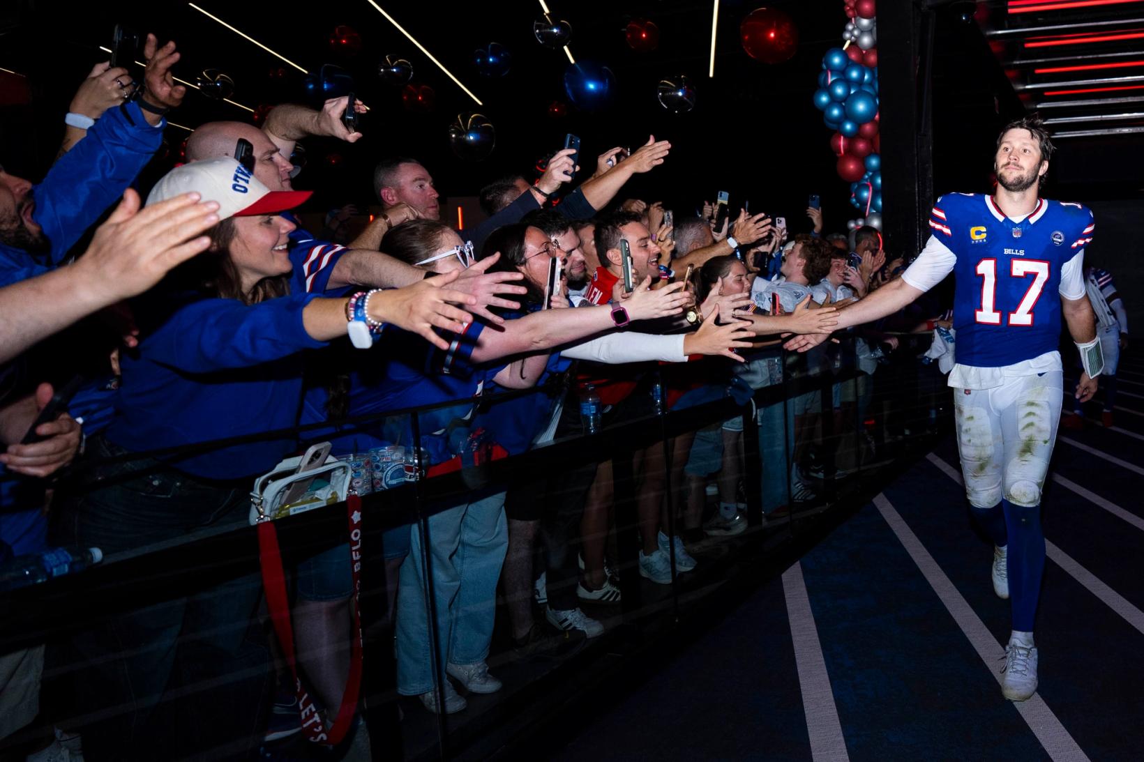 Buffalo Bills quarterback Josh Allen (17), his white pants grass-stained, slaps hands with cheering fans lining a tunnel at Highmark Stadium.