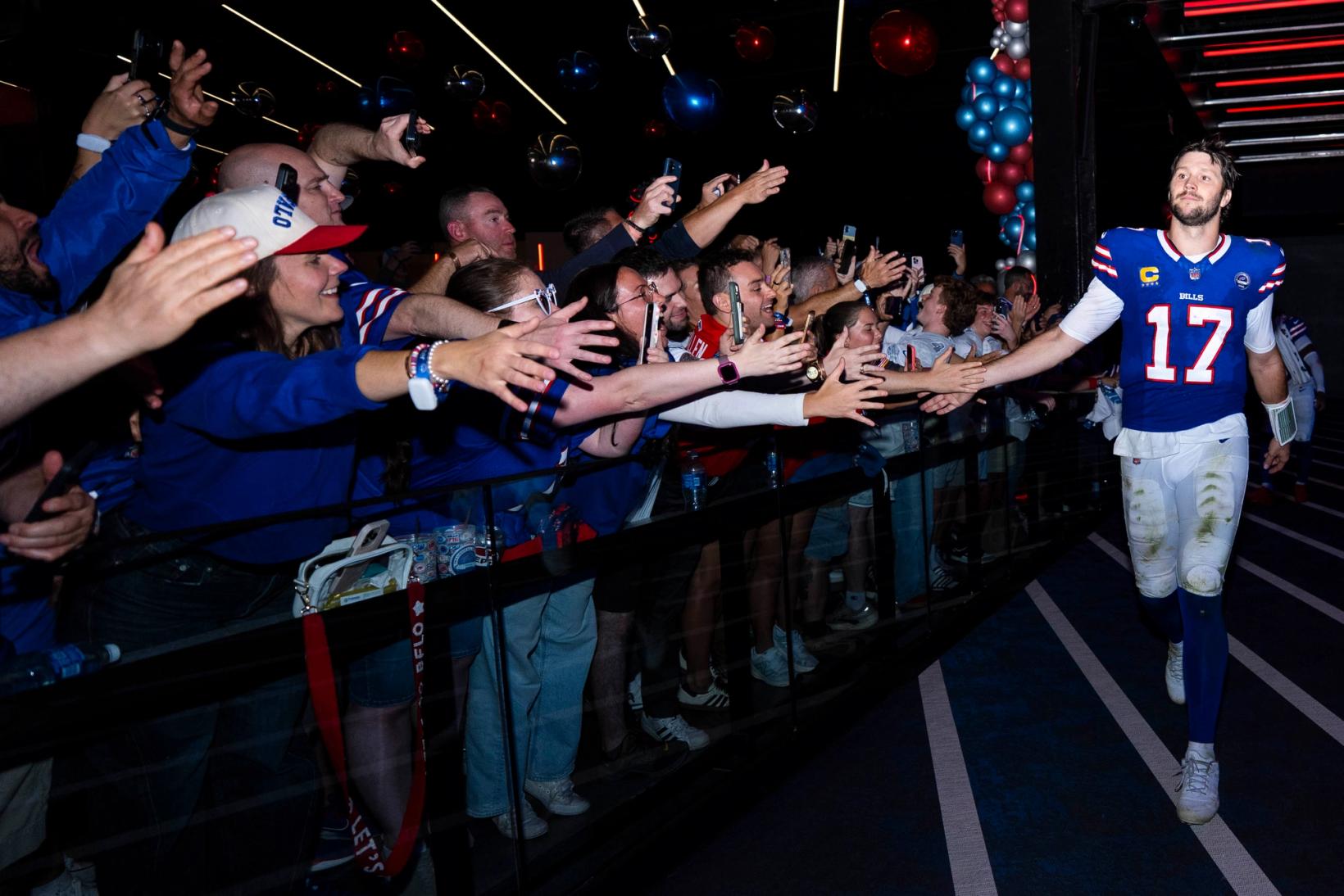 Buffalo Bills quarterback Josh Allen (17), his white pants grass-stained, slaps hands with cheering fans lining a tunnel at Highmark Stadium.