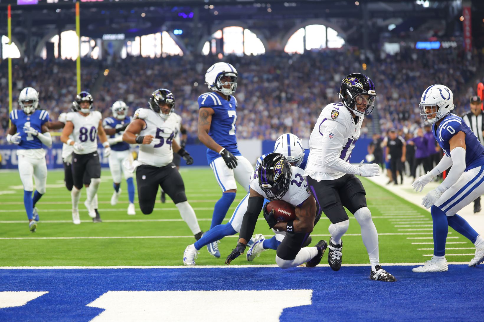 Baltimore Ravens running back Derrick Henry (22) clutches the football as he drives toward the goal line at Lucas Oil Stadium, surrounded by Indianapolis Colts defenders and Ravens teammates