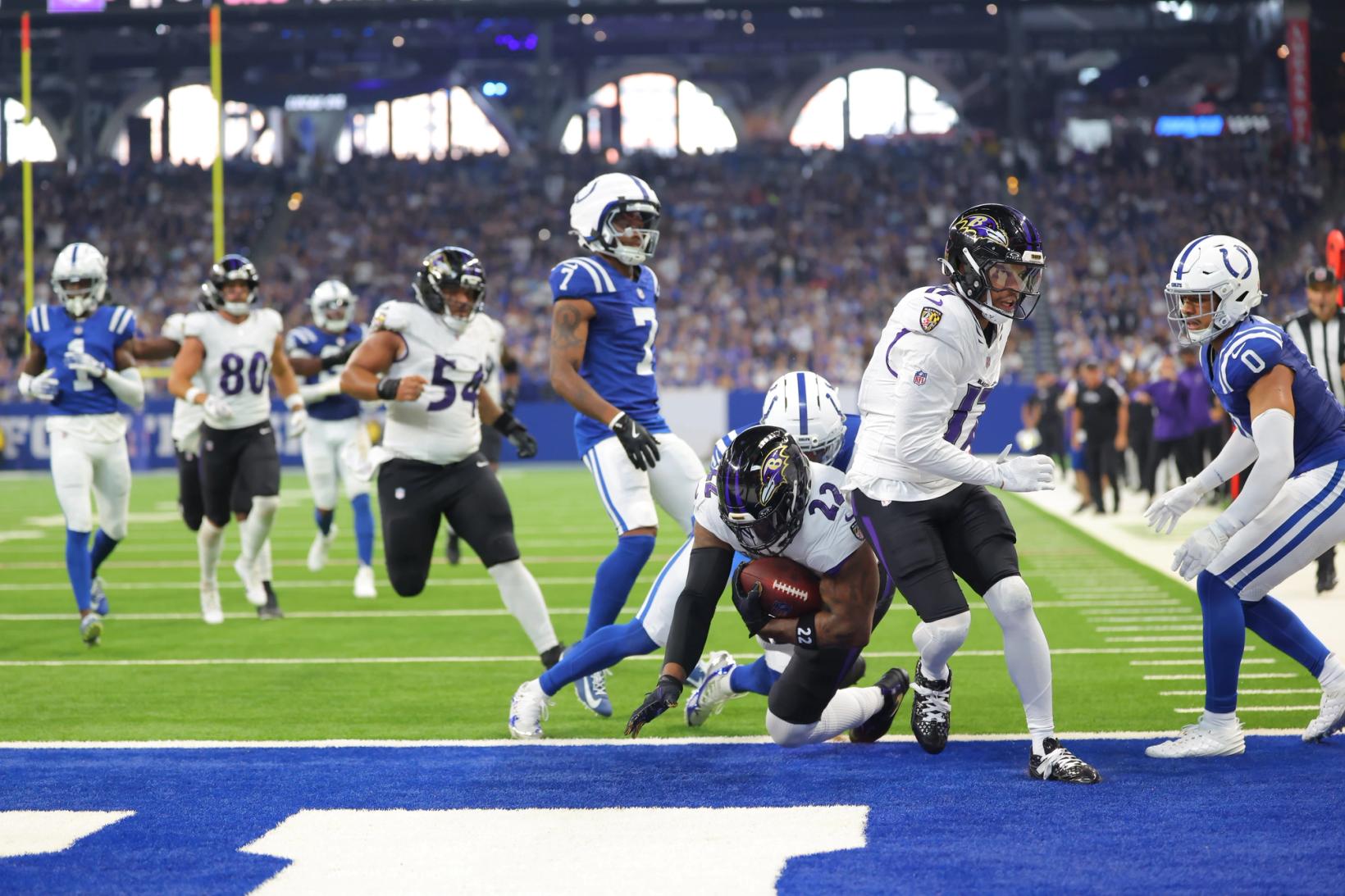 Baltimore Ravens running back Derrick Henry (22) clutches the football as he drives toward the goal line at Lucas Oil Stadium, surrounded by Indianapolis Colts defenders and Ravens teammates