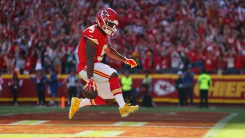 Kansas City Chiefs running back Kenneth Walker III (9) leaps in the end zone with the ball as Chiefs fans cheer behind him.