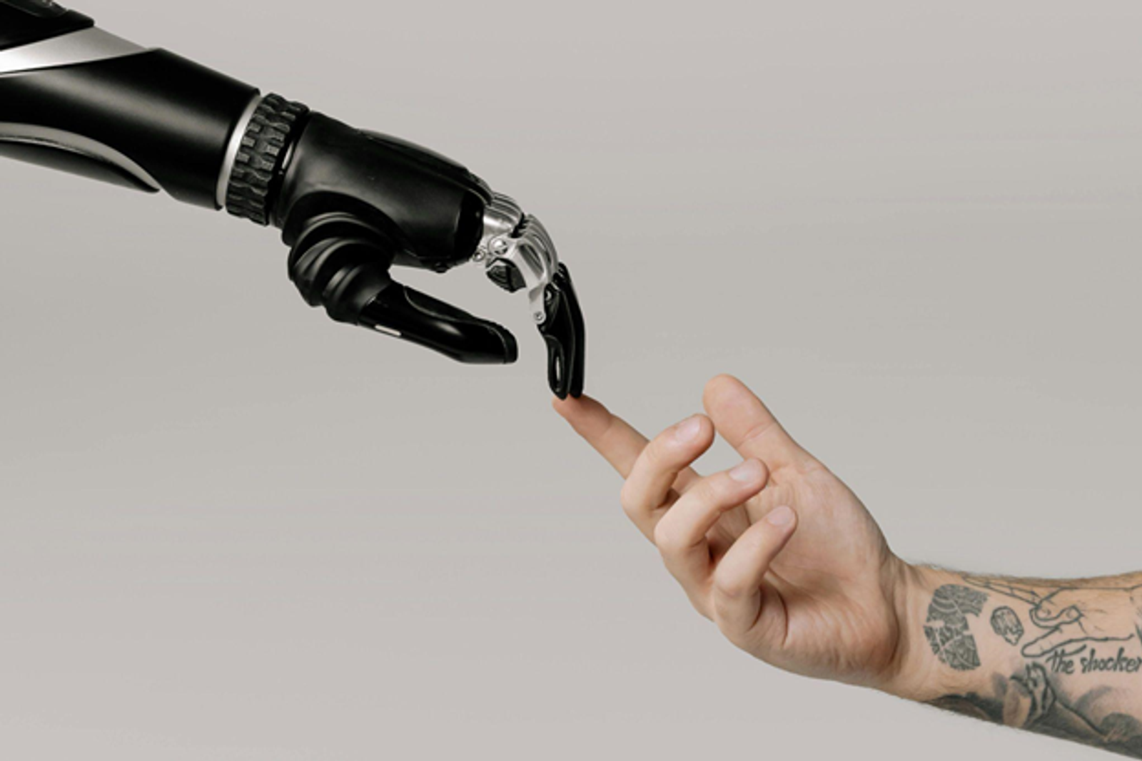 Robotic hand and human hand reaching toward each other, fingertips touching