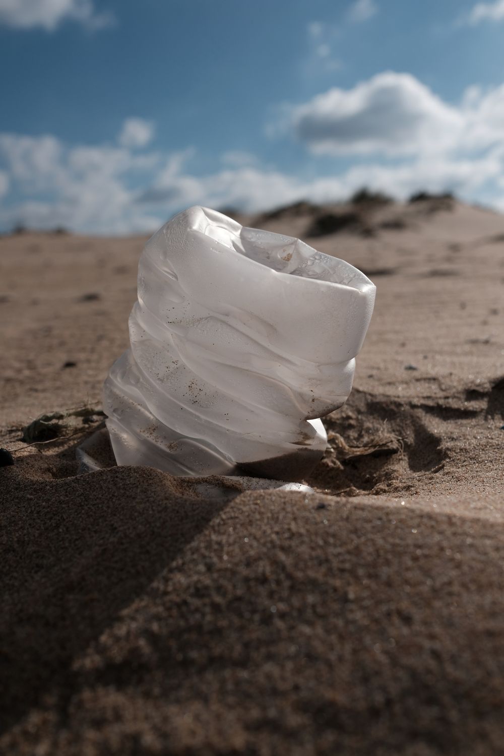 Empty plastic bottle buried in sand.
