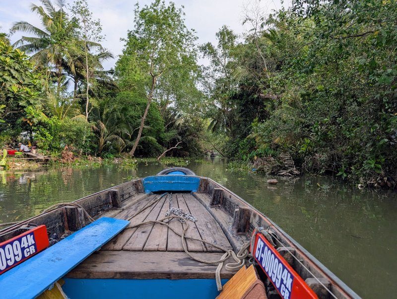 Balade en barque traditionnelle à travers un canal bordé de palmiers et de végétation dense à Can Tho