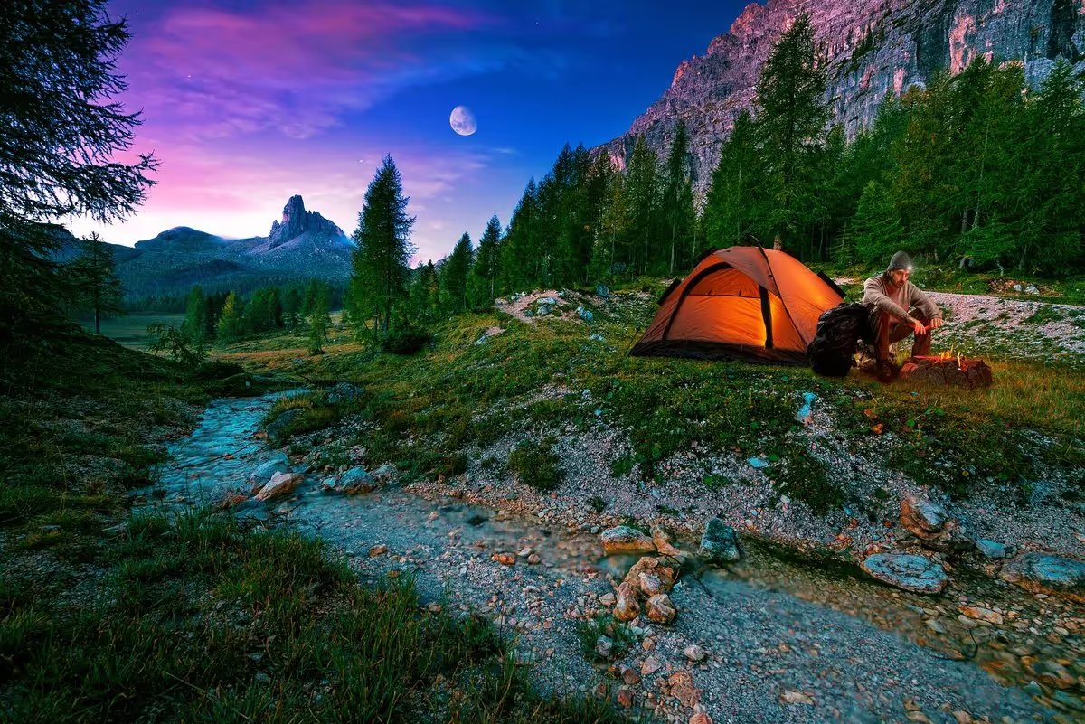 Homme en bivouac au bord d’un ruisseau en montagne, sous une tente éclairée au crépuscule