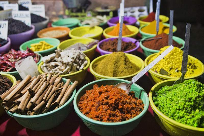 Assortiment coloré d’épices dans des bols au marché, incluant cannelle, curcuma, piments et mélanges en poudre.