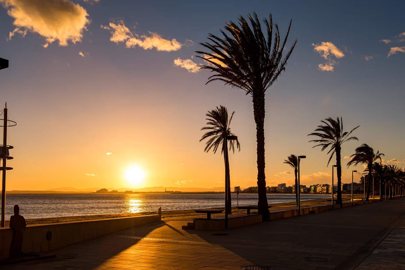 Promenade au coucher du soleil à Roses en Espagne avec des palmiers le long de la plage.