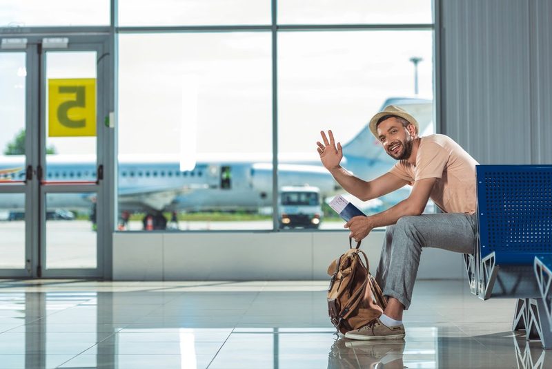 Voyageur souriant assis à l'aéroport avec son sac à dos, prêt à partir pour un voyage de dernière minute