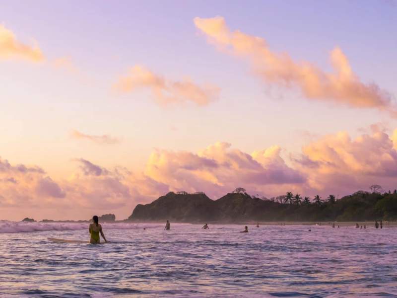 Surfeurs dans les eaux calmes de Playa Guiones au coucher du soleil, Nosara, Costa Rica.